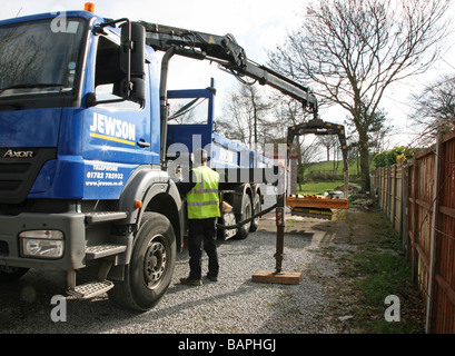 Un marchand de constructeur fournissant des panneaux de clôture en bois avec un camion avec un bras de levage hydraulique Banque D'Images