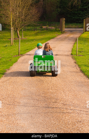 Un jeune garçon et fille jouant sur une batterie powered ride sur toy jeep descendre une route privée dans le pays Banque D'Images