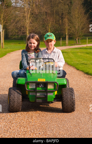 Un jeune garçon et fille jouant sur une batterie powered ride sur toy jeep descendre une route privée dans le pays Banque D'Images