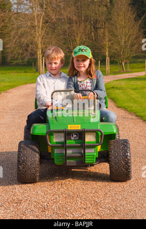 Un jeune garçon et fille jouant sur une batterie powered ride sur toy jeep descendre une route privée dans le pays Banque D'Images