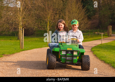 Un jeune garçon et fille jouant sur une batterie powered ride sur toy jeep descendre une route privée dans le pays Banque D'Images