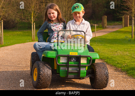 Un jeune garçon et fille jouant sur une batterie powered ride sur toy jeep descendre une route privée dans le pays Banque D'Images