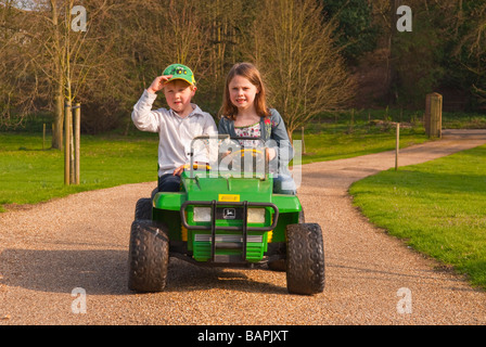 Un jeune garçon et fille jouant sur une batterie powered ride sur toy jeep descendre une route privée dans le pays Banque D'Images