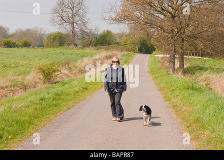 Une femme promener son chien seul le long d'un chemin de campagne du Suffolk, Royaume-Uni Banque D'Images