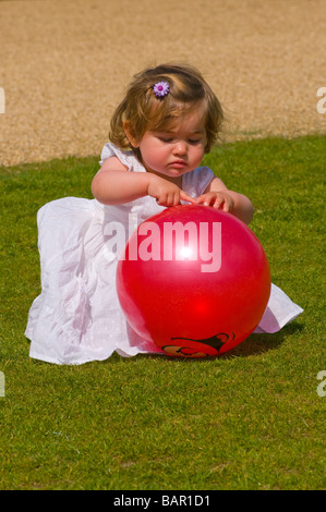 Jeune fille enfant jouant avec une balle de plastique rouge dans une robe d'été Banque D'Images