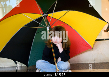 Petite fille s'ennuyer assis sur le sol sous un grand parapluie à l'intérieur du centre commercial Overgate à Dundee UK Banque D'Images