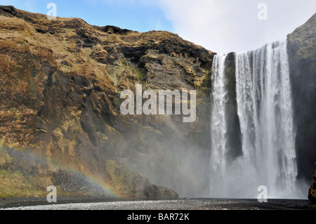 Vue frontale, grand angle de la cascade de Skogafoss, avec un arc-en-ciel dans le jet au pied, Skogar, le sud de l'Islande Banque D'Images