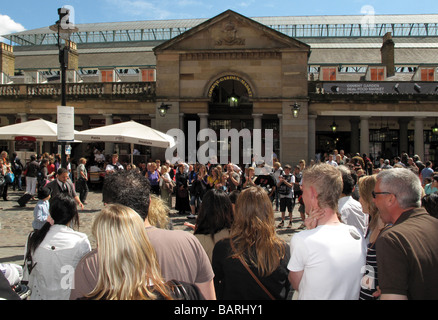 Des foules de touristes à regarder les artistes de rue de la rue au soleil à l'extérieur du marché de Covent Garden à Londres. Banque D'Images