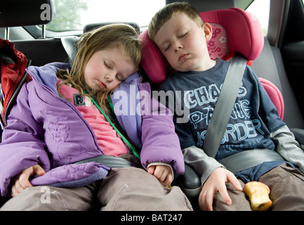 Les enfants dormant dans des sièges de voiture à l'arrière d'une voiture pour un voyage d'une journée. Banque D'Images