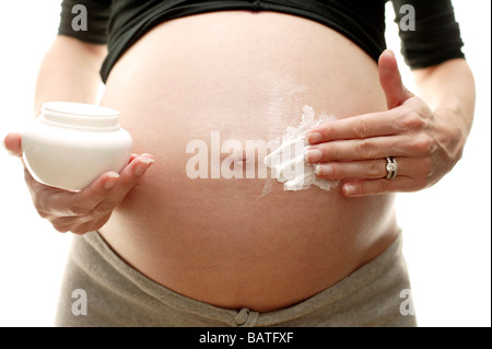 Femme enceinte l'application de la crème sur son abdomen gonflé. Garder la peau souple par moisturing aide à diminuer les vergetures. Banque D'Images