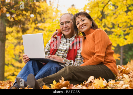 Young Woman using laptop sitting in autumn leaves Banque D'Images