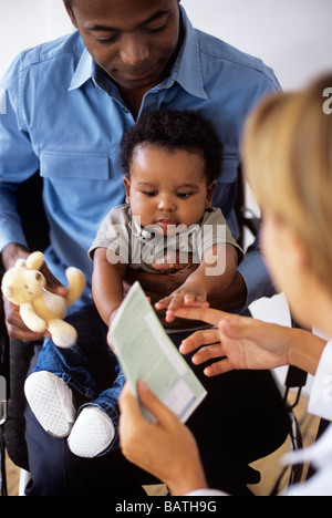 L'examen pédiatrique. Doctor prescription alors qu'elle examine un 5-month-old boy sitting in son père lap Banque D'Images