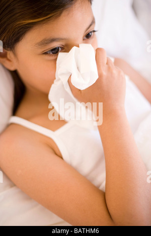 Girl blowing her nose tandis qu'elle est au lit. La rhinite allergique peut être provoquée par le froid commun. Banque D'Images