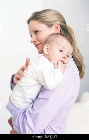 La mère et le bébé. Mère tenant son bébé fille qui est de sucer son pouce. Banque D'Images