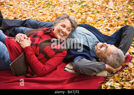 African couple laying on blanket parmi les feuilles d'automne Banque D'Images