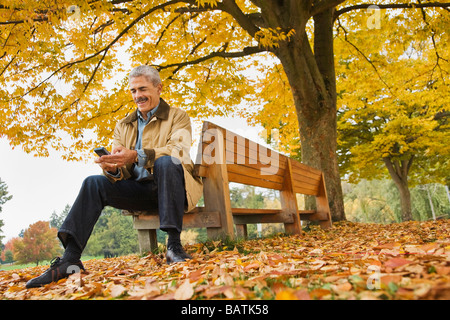African man using cell phone on banc de parc en automne Banque D'Images