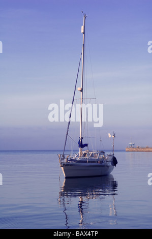 Un yacht solitaire début flottant sur un soir les eaux calmes à l'entrée du port de Weymouth, dans le Dorset, Angleterre. Banque D'Images