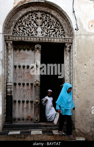Fille et garçon marchant à travers une porte en bois sculpté Zanzibari Banque D'Images