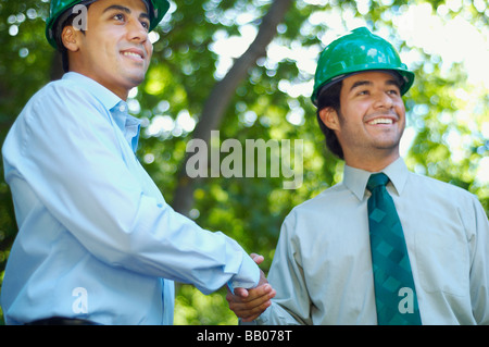 Business People in green hard hats shaking hands outdoors Banque D'Images