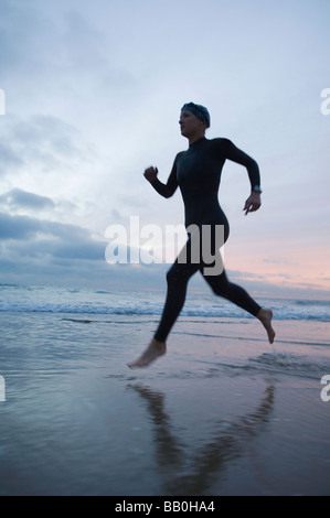 Hispanic woman in wetsuit running on beach Banque D'Images