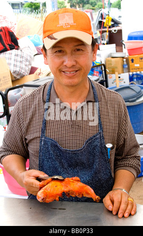 Asiatique Hmong chef holding un morceau de poulet rôti pour le restaurant en plein air. Sports Hmong Festival St Paul Minnesota USA Banque D'Images