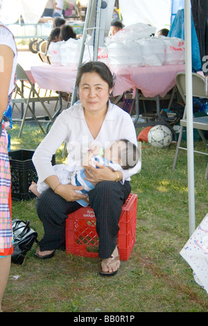 Maman de prendre un moment de l'animation de restaurant en plein air de donner son bébé une bouteille. Sports Hmong Festival St Paul Minnesota USA Banque D'Images