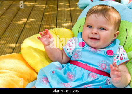 L'horizontale close up portrait of a cute baby girl à l'âge de six mois, assis sur un coussin coloré dans le jardin sur une journée ensoleillée Banque D'Images