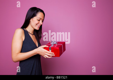 Woman smiling comme elle reçoit un cadeau enveloppé dans du papier cadeau rouge avec ruban d'argent et de cadeaux bow Banque D'Images