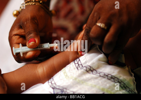 Les mains noires avec des squames sur le polonais rouge ongles tenant une seringue prépare à donner une injection Banque D'Images
