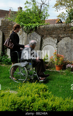 Un homme âgé en fauteuil roulant poussé autour d'un cimetière par son soignant féminin Banque D'Images