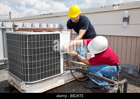 Deux travailleurs sur le toit d'un bâtiment de travailler sur l'appareil de climatisation Banque D'Images