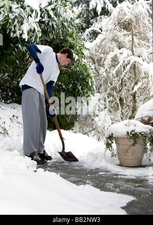 Un jeune homme de pelles neige sur un trottoir. Banque D'Images