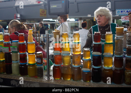 Un vendeur de miel sur le marché de Zhytni dans la région de Podol à Kiev (Kiev) en Ukraine. Des pots de hoiney de couleur jaune, orange, rouge attendent les clients Banque D'Images