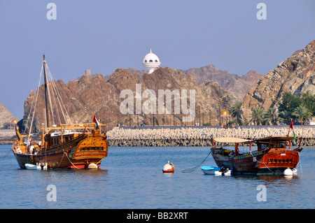 Muscat Oman dhows amarré dans le port de Muttrah avec une tour de guet de brûleur d'encens sur la chaîne de montagnes Hajar au-delà des défenses maritimes côtières Banque D'Images