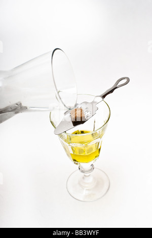 Une bouteille en verre de l'eau glacée coulée sur un verre d'absinthe à travers un morceau de sucre posé sur une cuillère à absinthe Banque D'Images