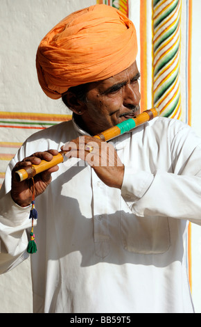 Un homme avec une moustache et un turban orange joue une flûte de bambou Banque D'Images