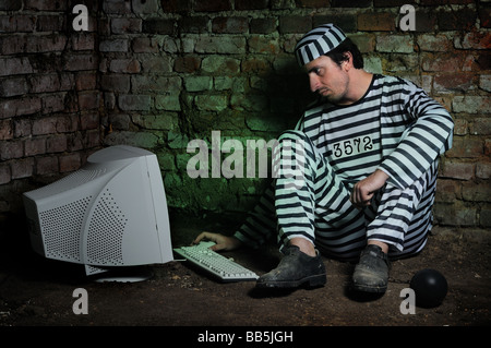 Prisonnier dans une cellule sombre de travailler avec l'ordinateur. Banque D'Images