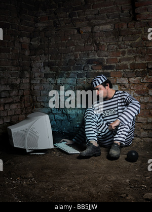 Prisonnier dans une cellule sombre de travailler avec l'ordinateur. Banque D'Images