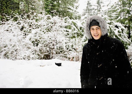 Mixed Race man en manteau à capuchon extérieur dans la neige Banque D'Images