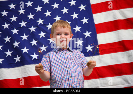 Jeune garçon waving sparklers in front of American flag Banque D'Images