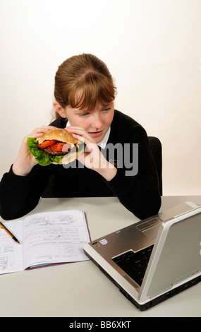 Manger une écolière beefburger avec une salade saine tout en faisant ses devoirs de remplissage Banque D'Images