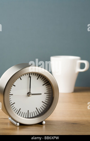 Une horloge indiquant trois heures avec une tasse de thé derrière Banque D'Images