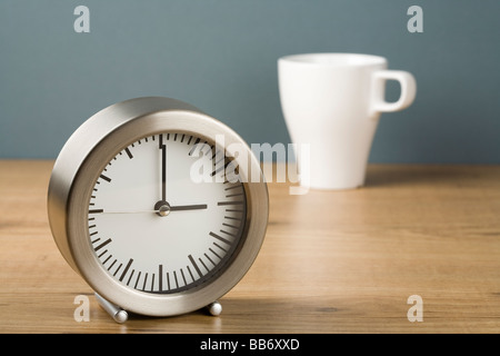 Une horloge indiquant trois heures avec une tasse de thé derrière Banque D'Images