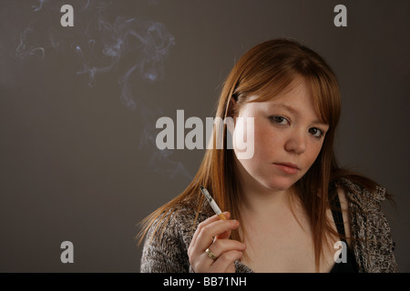 Jeune femme aux cheveux rouges tenant une cigarette allumée dans sa main . Banque D'Images