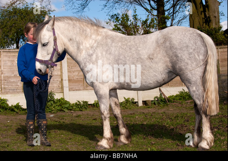 Blonde girl holding a white pony en paddock Cumbria Banque D'Images