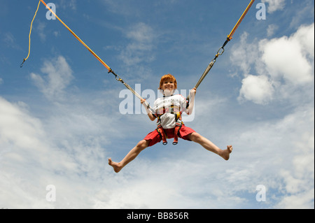 Jeune garçon sautant sur un trampoline bungee et voler dans l'air Banque D'Images