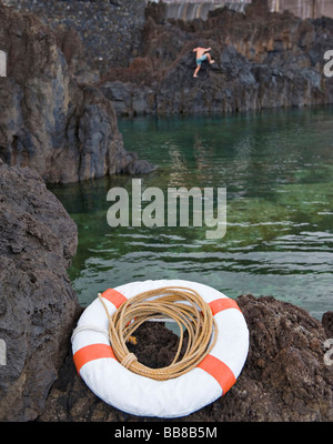 Lava-fait piscine naturelle, les bouées à l'avant et un homme escalade les rochers à l'arrière, Porto Moniz, Madeira, Portugal Banque D'Images