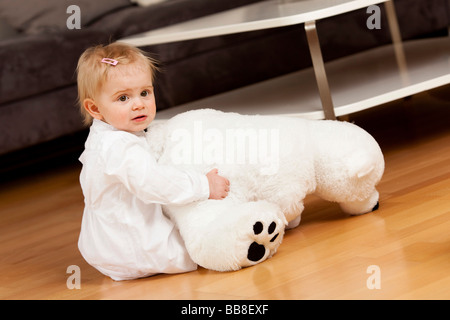 Jeune fille, 1 ans, jouant sur le plancher avec un jouet ours polaire Banque D'Images