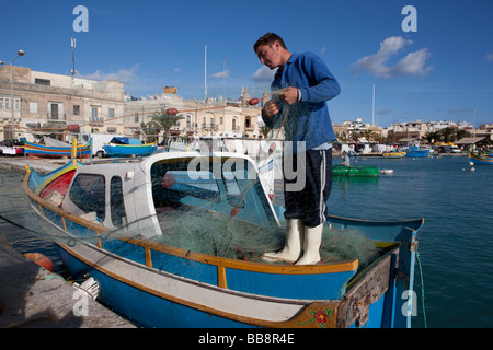 Pêcheur réparant son filet sur un bateau de pêche, le port de Marsaxlokk, Malte, Europe Banque D'Images