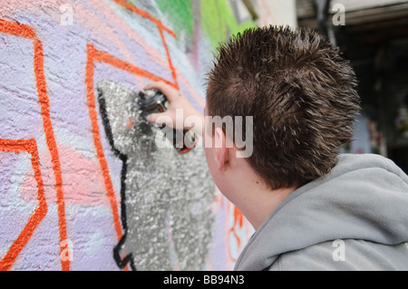 Teenage boy travaillant sur un morceau grafitti sur un mur extérieur. Banque D'Images